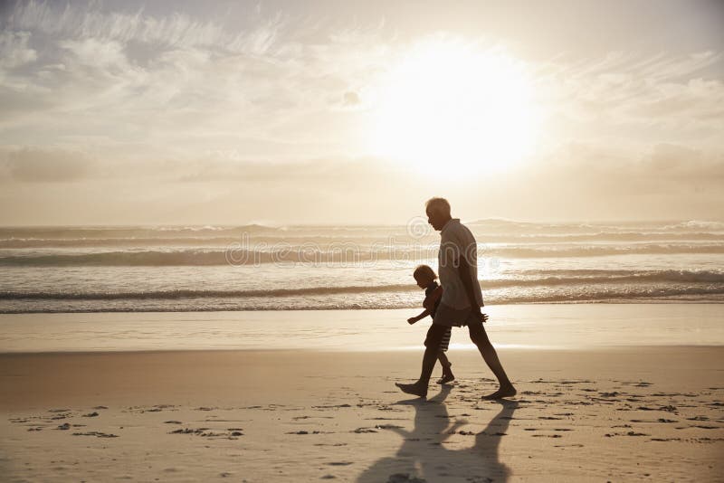 Silhouette Of Grandfather Walking Along Beach With Grandson