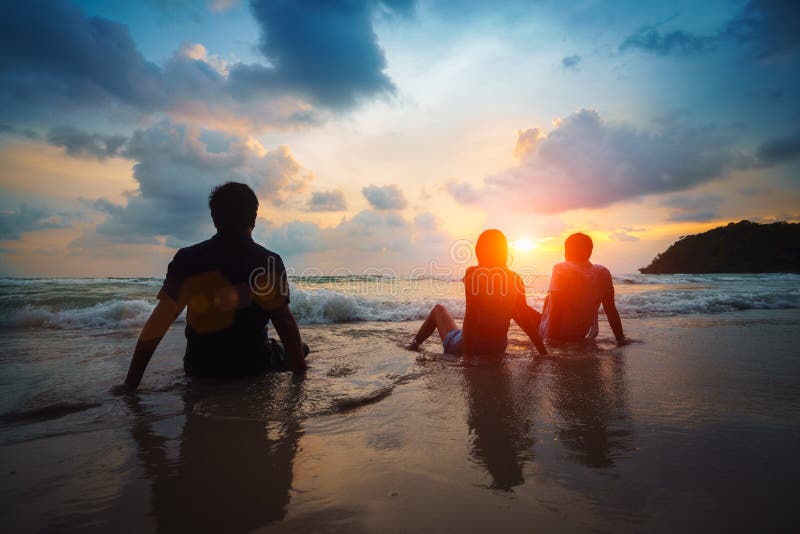 Silhouette-grupp med vänner som relaxerar på en strand medan solnedgången