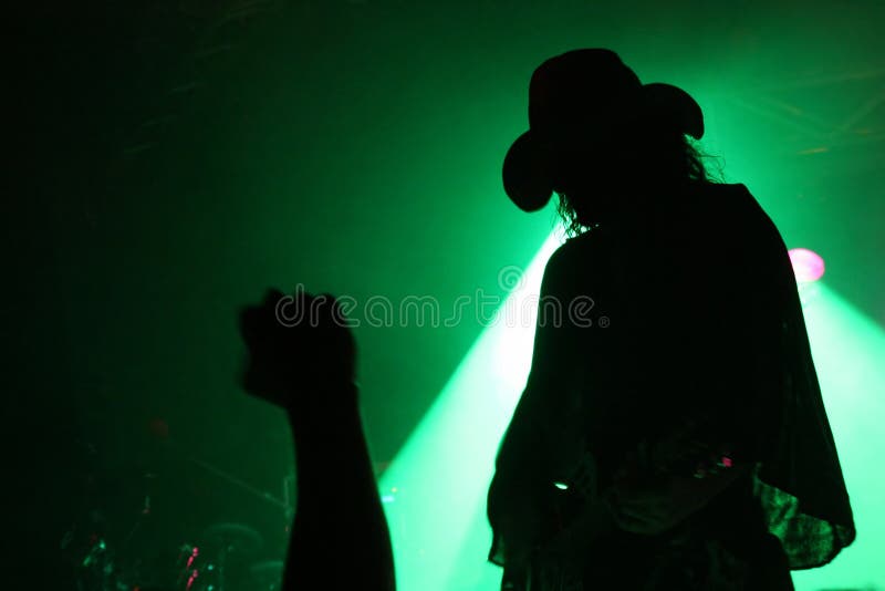 Silhouette of a guitarist on stage with a cowboy hat with fan s fist in front of green reflector