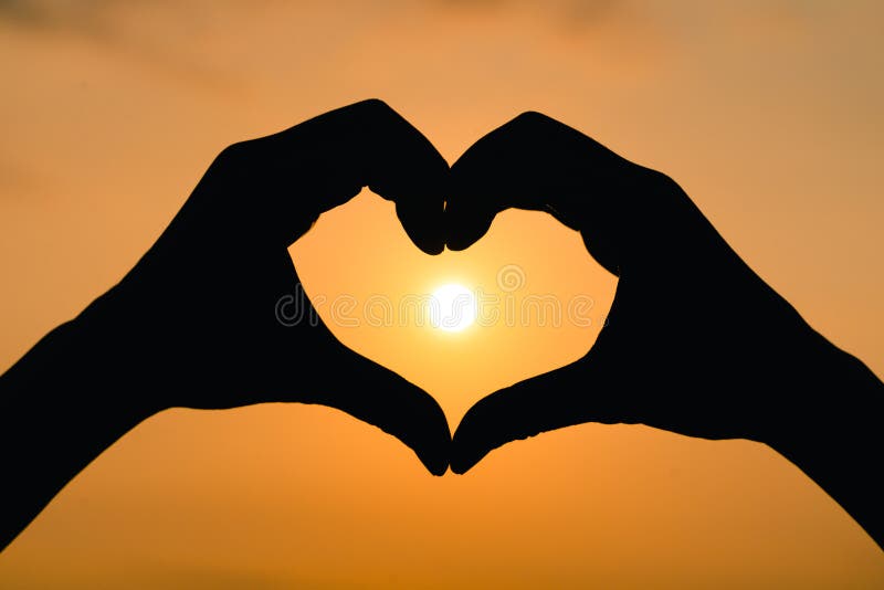 Silhouette hand in heart shape with sunrise on the sky background. love concept