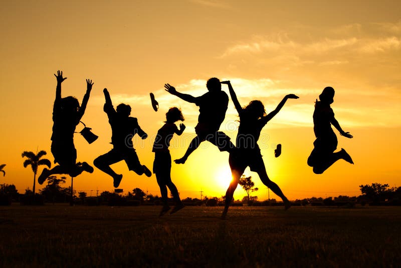 Silueta saltando adolescentes a través de cálido oscuridad el cielo.