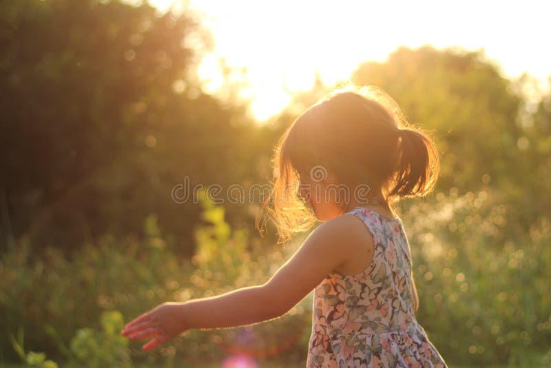 silhouette of a little girl with a ponytail in a flower dress outdoors in the rays of sunny sunset