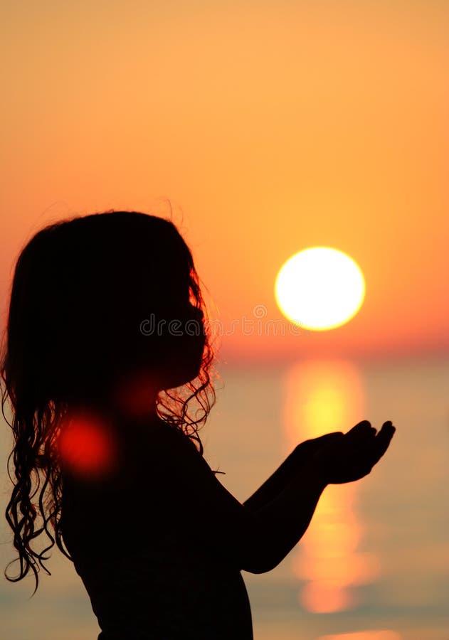 Silhouette of little girl at the sea holding the sun