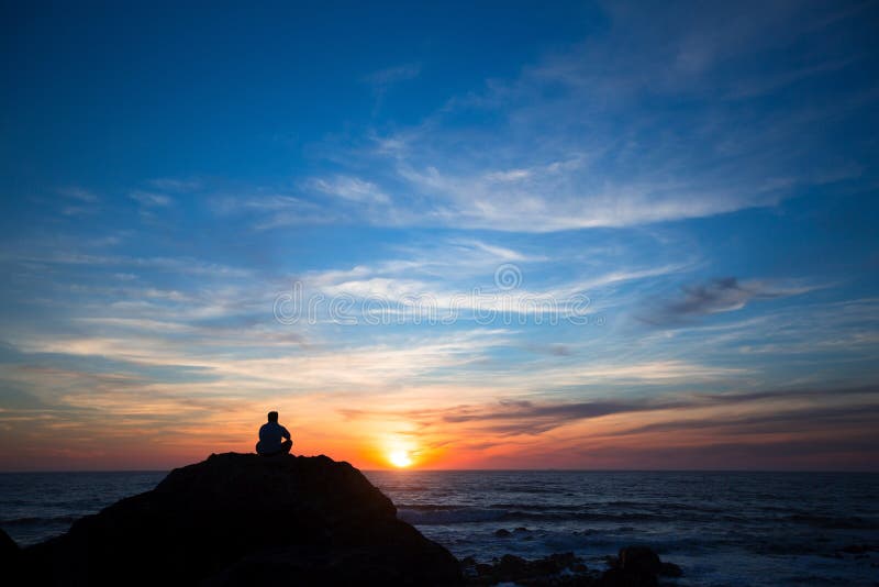 Silhouette of a lonely man sitting on the rocks at ocean beach