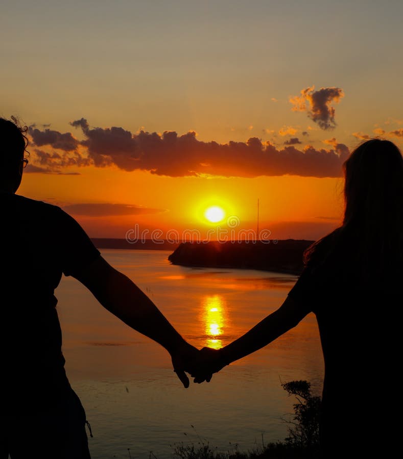 Silhouette Of Romantic Couple Holding Hands On The Beach And Looking At Sunset Over The Sea