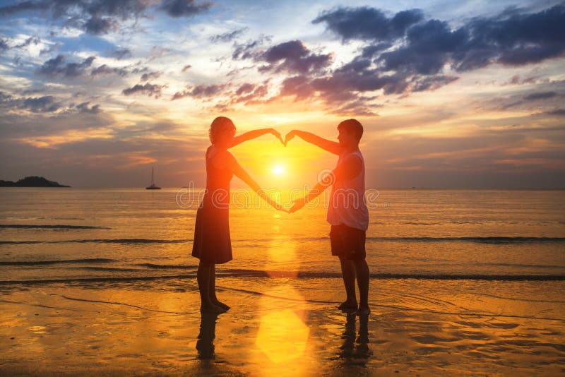 Silhouette of loving couple during an amazing sunset, holding hands in heart shape. Love.