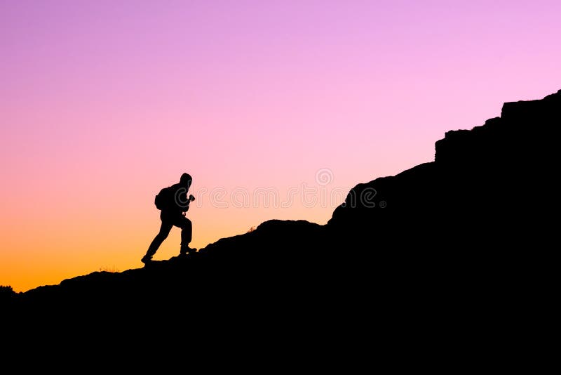 The silhouette of a man climbing a mountain in the sunset light