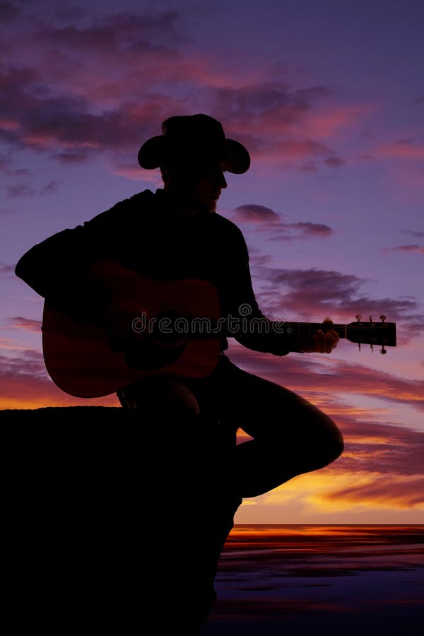 Silhouette of man with guitar sit by water sunset