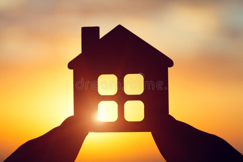 silhouette of man`s hand holding small wooden house against sunset or sunrise light