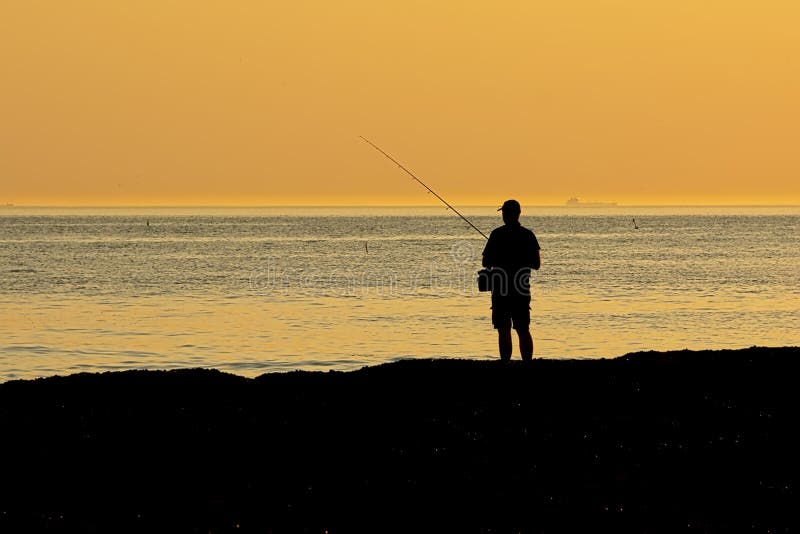 Silhouette of a man standing,fishing in the sea in orange evening light