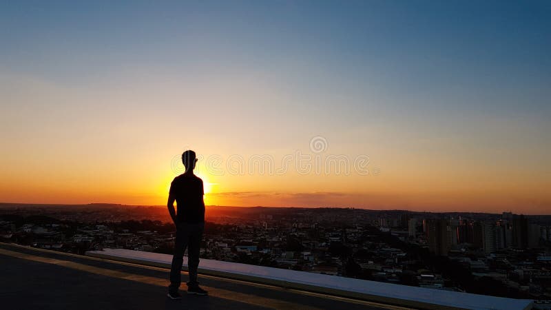 Silhouette of a man on top of a building. Sunset on the city in the background