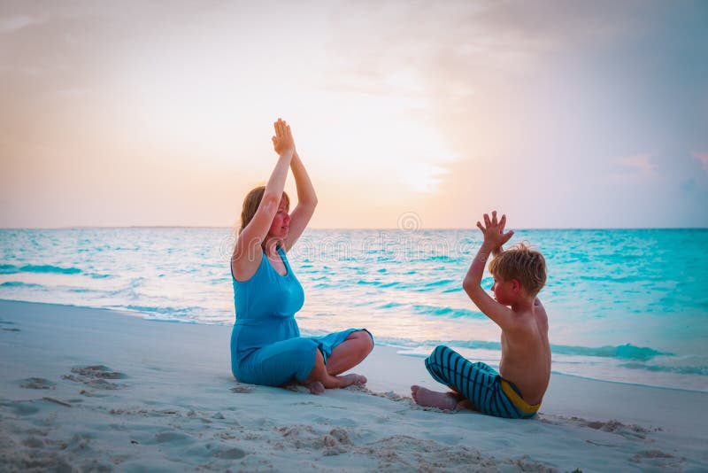 Silhouette of mother and son doing yoga on beach. 