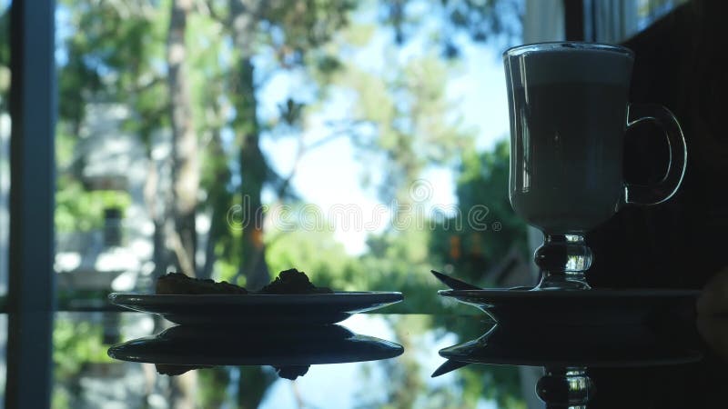 Silhouette non reconnue de femme se reposant avec le verre du cappuccino et du gâteau banque de vidéos