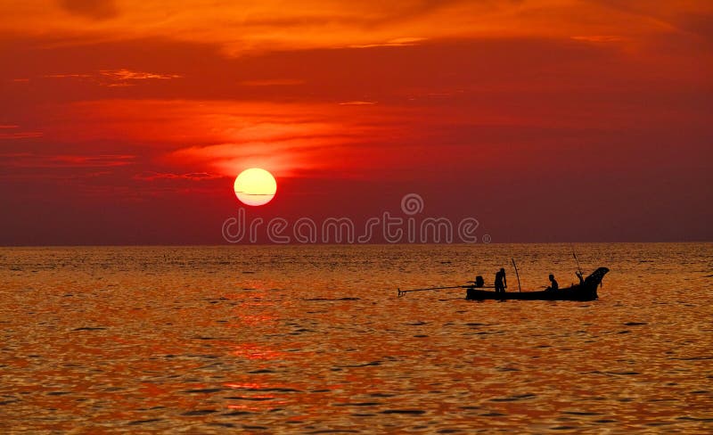 Silhouette of people on a boat sailing in the water with sun in the red sky