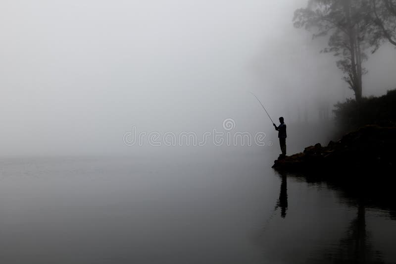 Silhouette of a person fishing near a lake with reflection and surrounded by fog and mist.