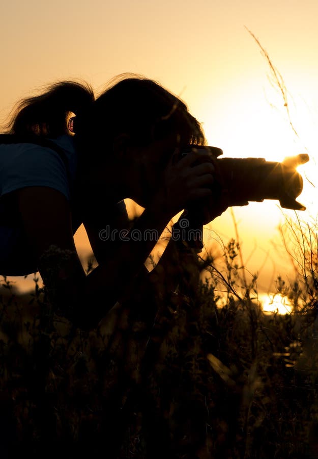 Silhouette portrait of a young woman photographing a beautiful nature at sunset on photo equipment