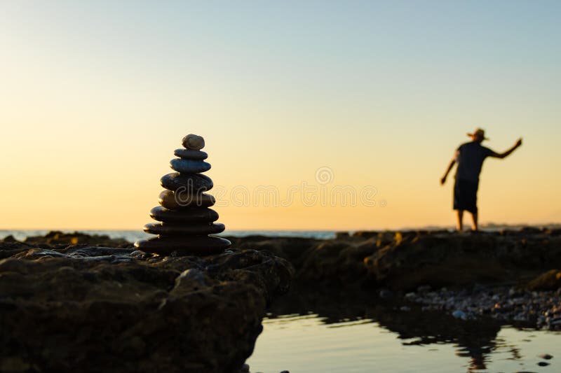 Silhouette of a pyramid of pebbles and a blurred man throwing stones into the sea. royalty free stock image