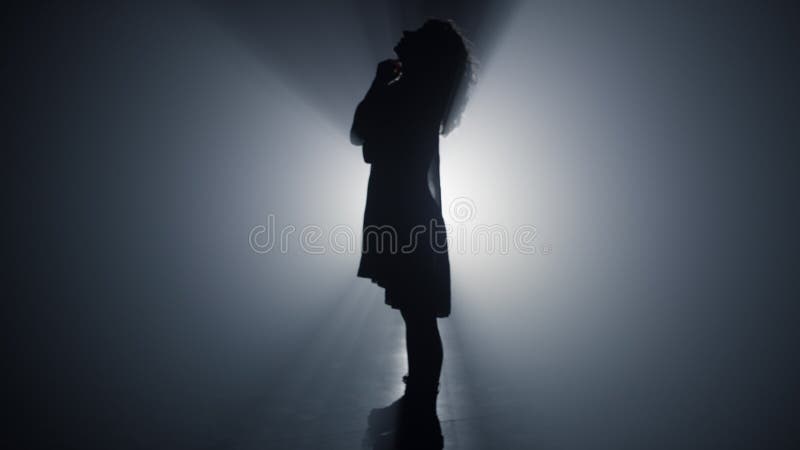 Silhouette slim woman looking up indoors. Beautiful girl standing in dark space.