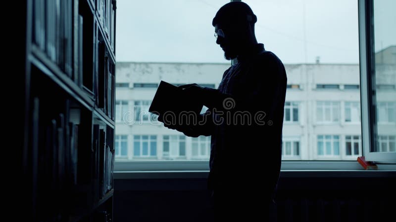 Silhouette studentessa di sesso maschile esamina i libri della biblioteca universitaria leggendo