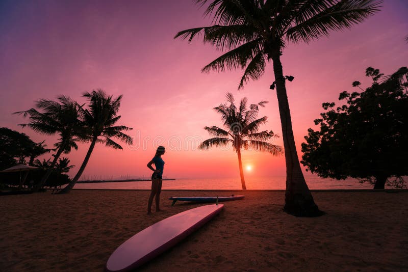 Silhouette of surfer girl with long surf board at sunset on tropical beach