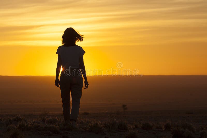 The magic light at sunset in the Namibian desert. Silhouette of a woman walking towards the setting sun. The magic light at sunset in the Namibian desert. Silhouette of a woman walking towards the setting sun.