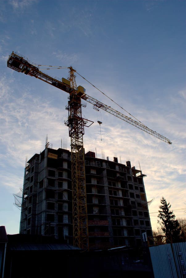 Silhouette of a tower crane and a high-rise building under construction against the background of the morning sky