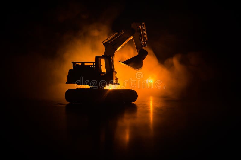 Silhouette tracked excavator on dark foggy red orange sky background with toy car. Empty space