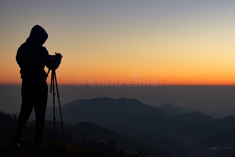 Silhouette of Travel photographer standing with a camera mounted on a tripod and shooting a time lapse