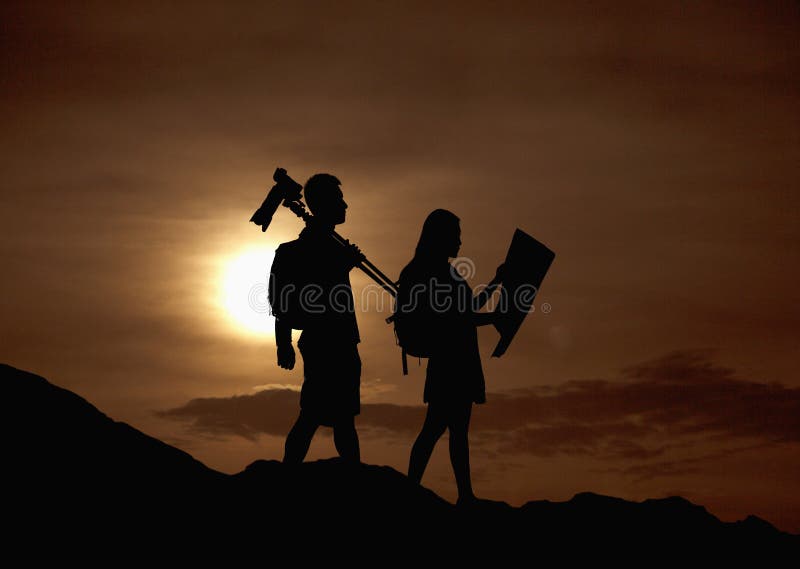 Silhouette of two people hiking and carrying camera and a map in nature at sunset