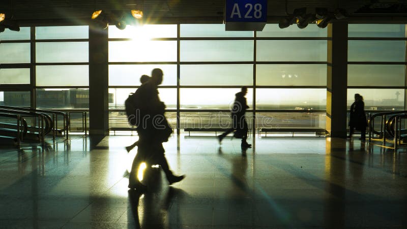 SILHOUETTE: Unrecognizable tourists hurry down an airport terminal at sunrise. stock photos