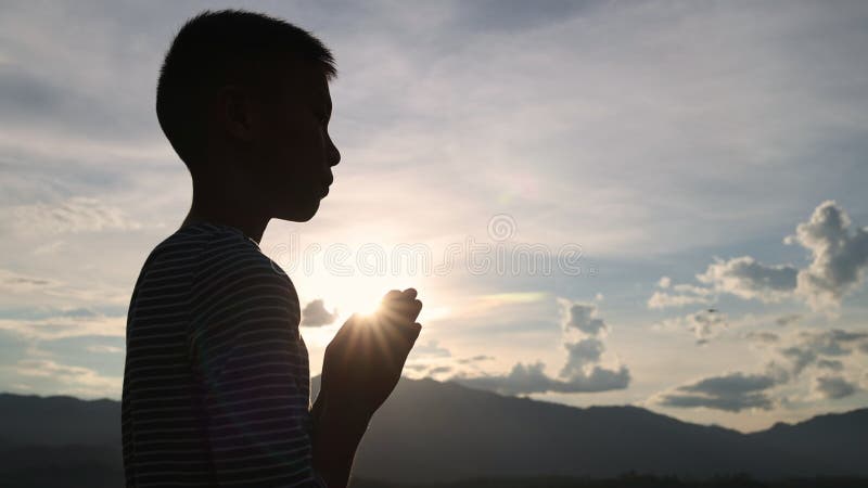 Silhouette van de jongen die bidt voor de zon en die het concept spiritualiteit en religie neerhaalt. religieuze overtuigingen. go