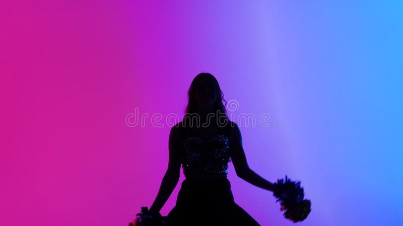 Silhouette von schlanken Cheerleader tanzen energisch mit Pompoms in den Händen vor dem Hintergrund der rosa blauen Lichter in stock video
