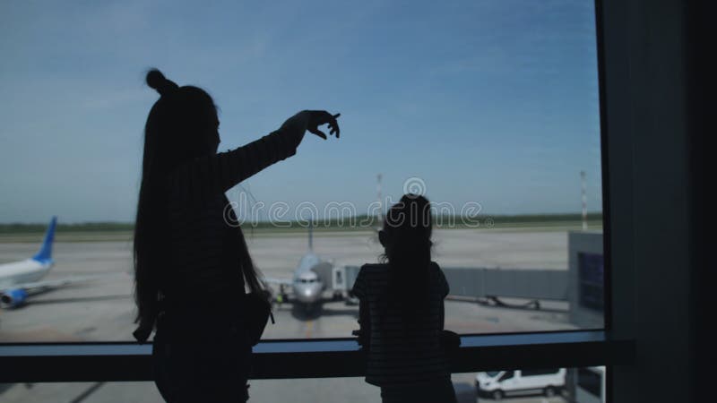 Silhouette von zwei Schwestern stehen am Fenster des Wartezimmers des Flughafens mit Blick auf das Flugzeug