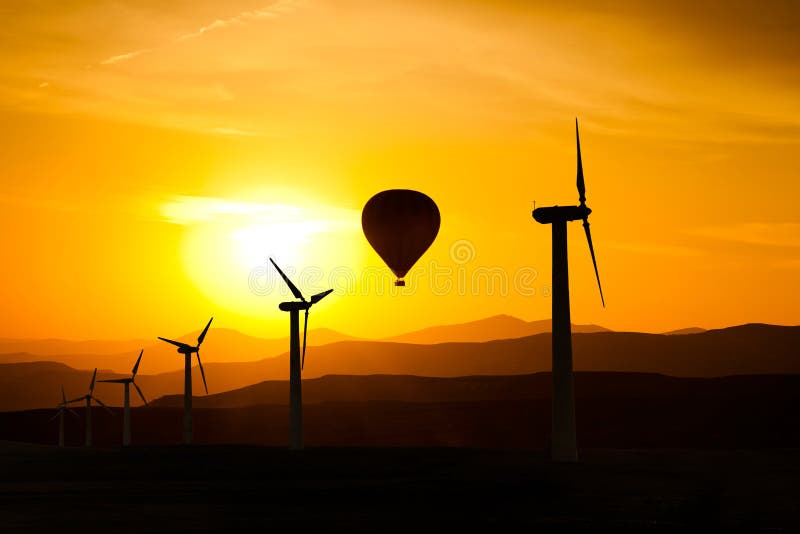 Silhouette of wind turbines and a hot air balloon f mountains and the sunset