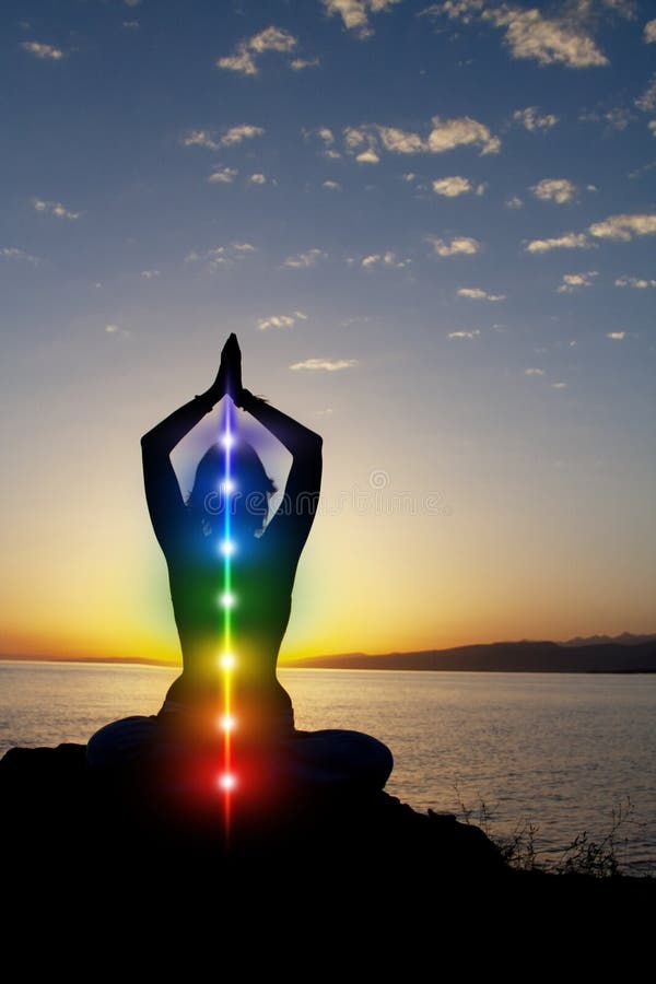 Silhouette of woman sits in a lotus pose on beach sunset view, glowing seven all chakra. Kundalini energy. girl practicing yoga