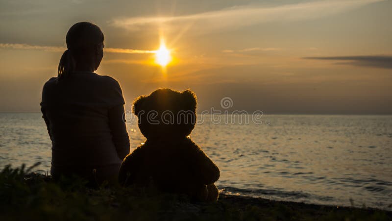 Silhouette of a woman and a teddy bear by the sea at sunset