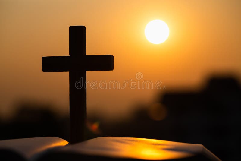 Silhouette of the wooden cross over opened bible with a bright sunrise as background , Christian, god.