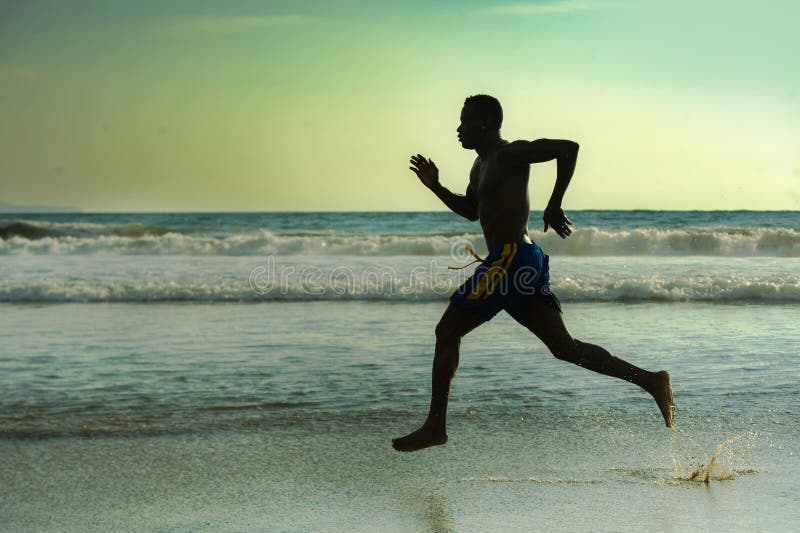 Silhouette of young attractive fit athletic and strong black African American man running at sunset beach training hard and