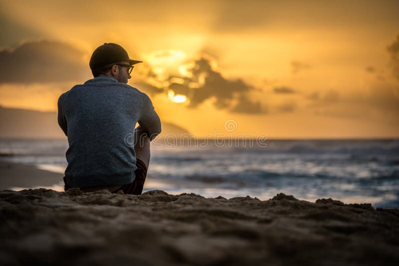 Silhouette of young caucasian male sitting on Sunset Beach looking out at sunset over the ocean