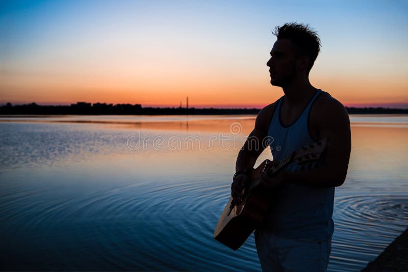 Silhouette of young handsome man playing guitar at seaside during sunrise. Outdoors. royalty free stock photo Silhouette of young handsome man playing guitar at seaside during sunrise. Outdoors. royalty free stock photo