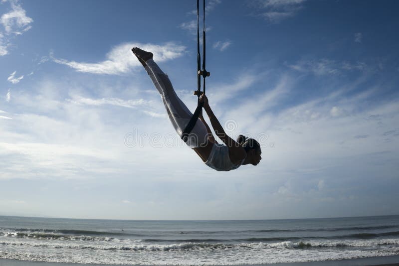 Silhouette of young happy and athletic Asian Indonesian woman doing aero yoga workout training body balance hanging from swing stock photo Silhouette of young happy and athletic Asian Indonesian woman doing aero yoga workout training body balance hanging from swing stock photo