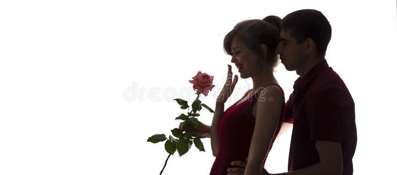 Silhouette of a young man and woman in love on white isolated background, boy came up behind to girl to make a surprise with rose stock image Silhouette of a young man and woman in love on white isolated background, boy came up behind to girl to make a surprise with rose stock image