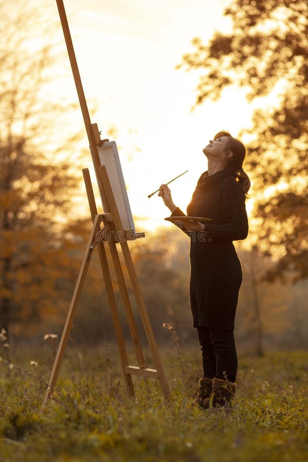 Silhouette of young woman artist painting a picture on the easel, girl figure with a brush and a palette of colors on the stock photography Silhouette of young woman artist painting a picture on the easel, girl figure with a brush and a palette of colors on the stock photography