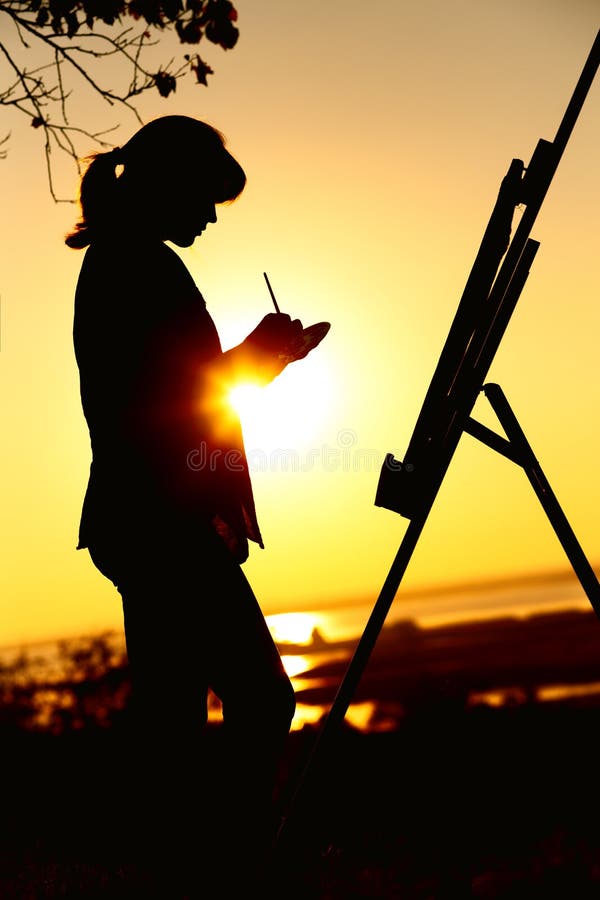 Silhouette of a young woman drawing a picture on an easel on nature, female standing under tree with brush and artist`s palette stock image Silhouette of a young woman drawing a picture on an easel on nature, female standing under tree with brush and artist`s palette stock image