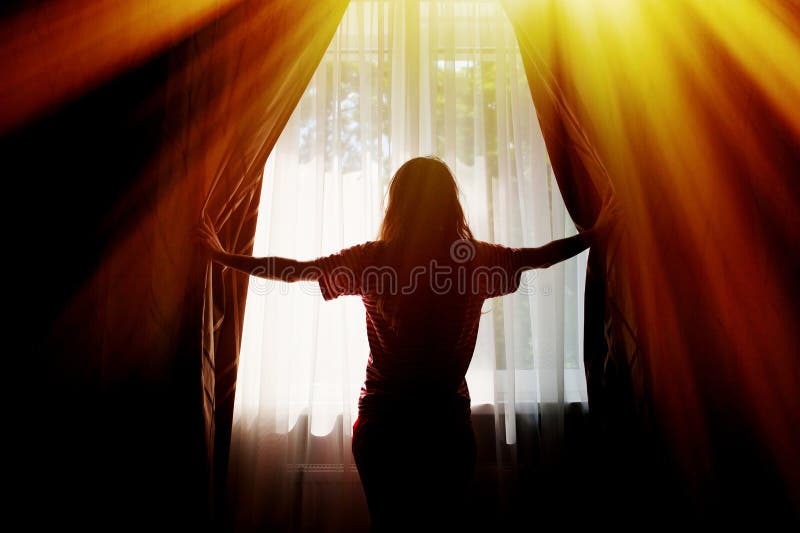 Silhouette of a young woman opens curtains at window.