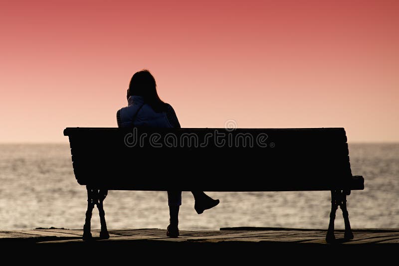 Silhouette of young woman sitting alone on the bench stock image Silhouette of young woman sitting alone on the bench stock image