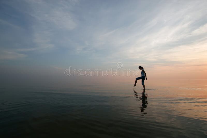 Silhouette of young woman wading in sea at sunset