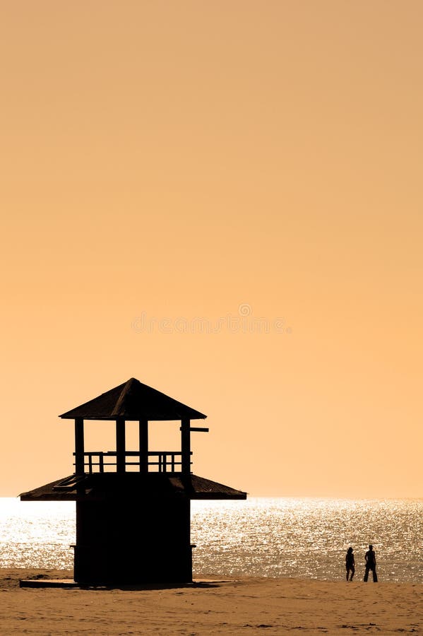 Silhouetted couple walking along beach at sunset