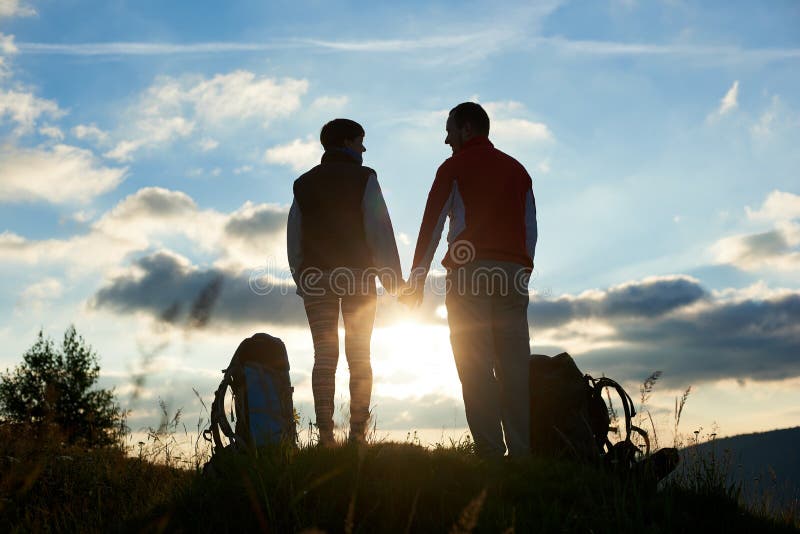 Silhouetten die van mens en vrouw die elkaar de bekijken, handen houden tegen zonsondergang in bergen royalty-vrije stock fotografie Silhouetten die van mens en vrouw die elkaar de bekijken, handen houden tegen zonsondergang in bergen royalty-vrije stock fotografie