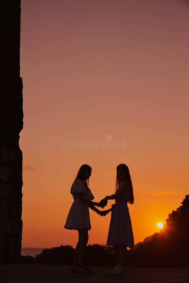 Silhouetten von zwei Mädchen vor dem Hintergrund des orangen Himmels und der untergehenden Sonne stockfotografie
